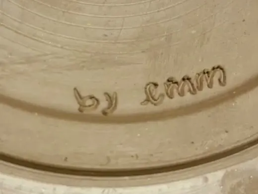 La firma «by emm» tallada con una aguja en la base de una pieza de barro.
