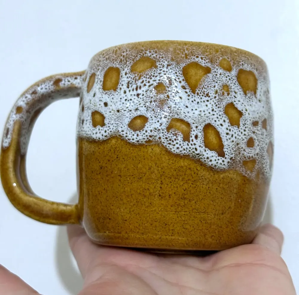 Taza color miel con un esmalte blanco burbujeante en la parte de arriba.