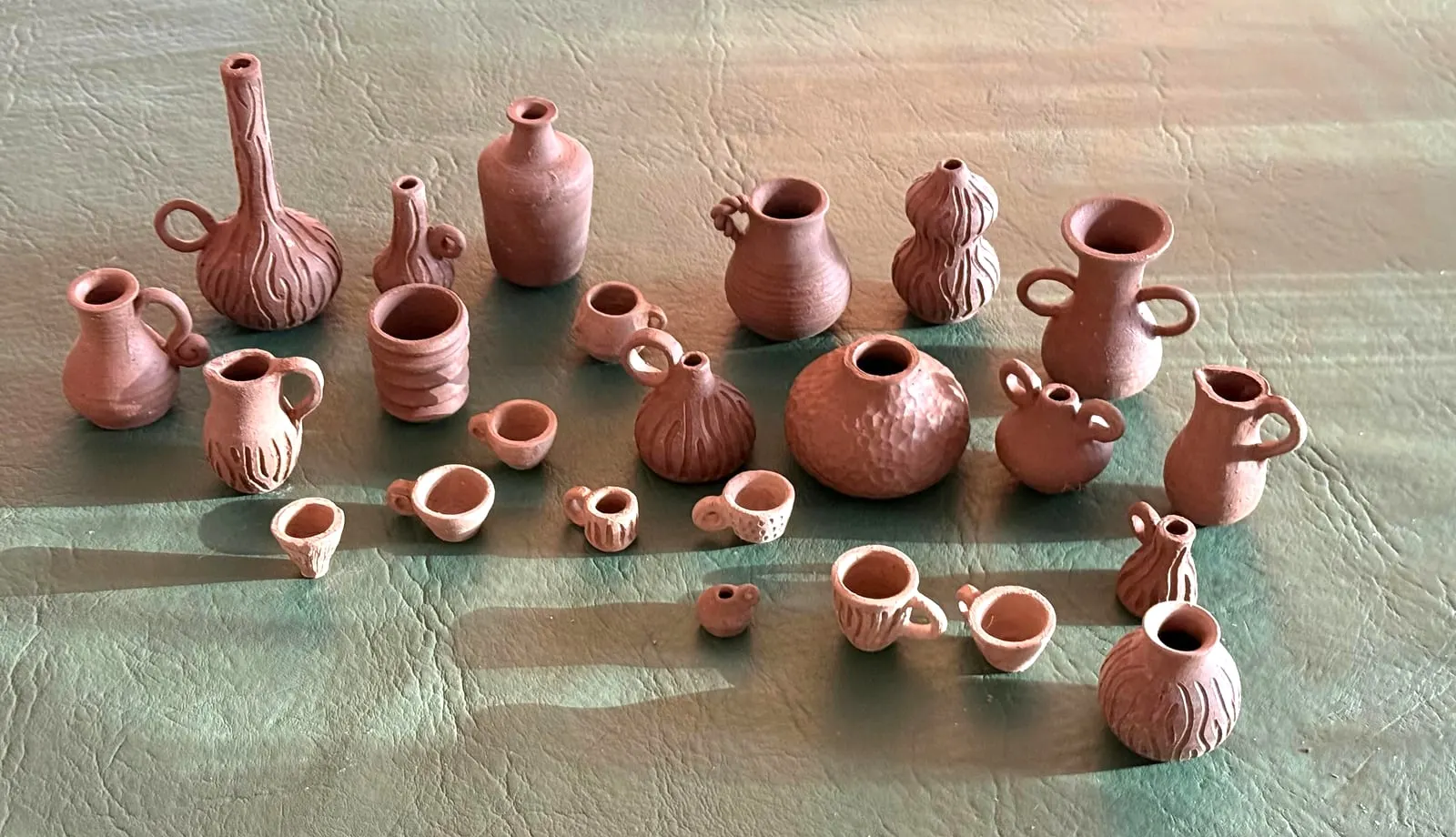 Unas veinticinco miniaturas de barro rojo sobre una mesa de cuero verde, con sombras largas de tarde.