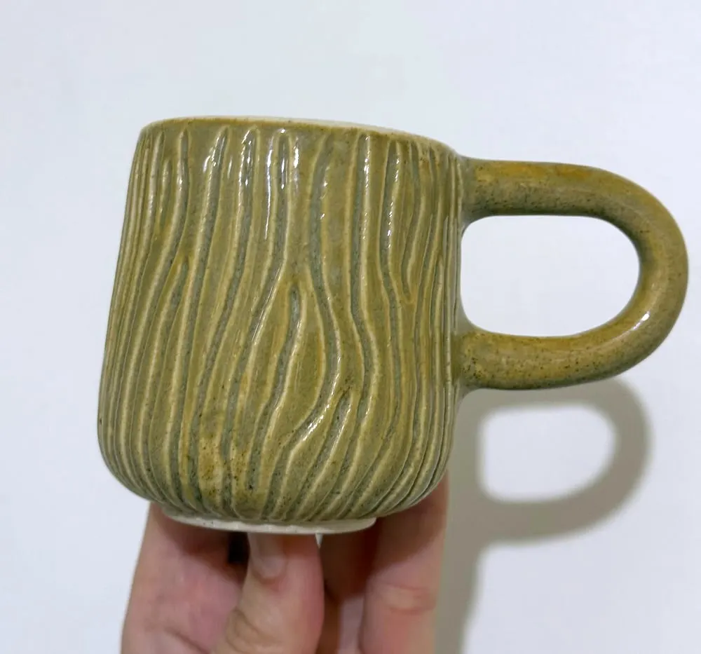 Taza verde oliva con líneas onduladas talladas y asa redonda.