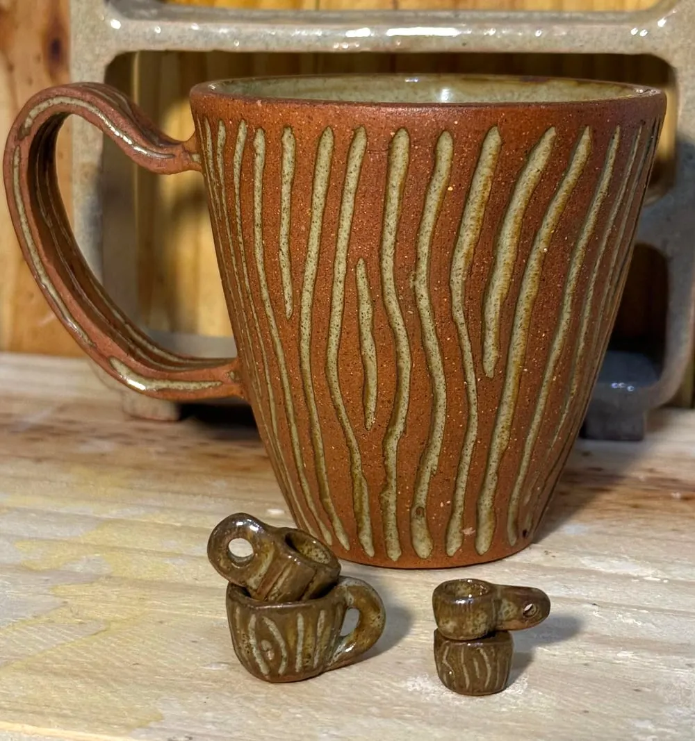 Taza de barro rojo con líneas claras talladas, junto a tres tacitas miniatura apiladas.