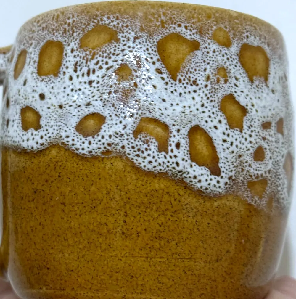 Detalle de un esmalte blanco que parece espuma sobre una taza color miel.